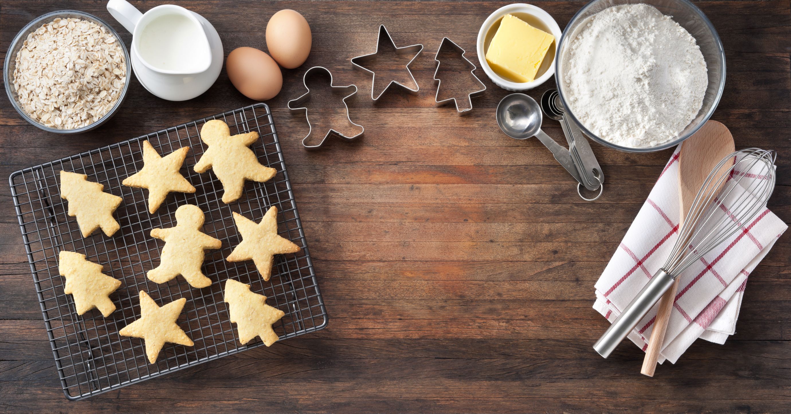 Christmas cookies with baking utensils, ingredients and cookie cutters on a rustic wood background from above.