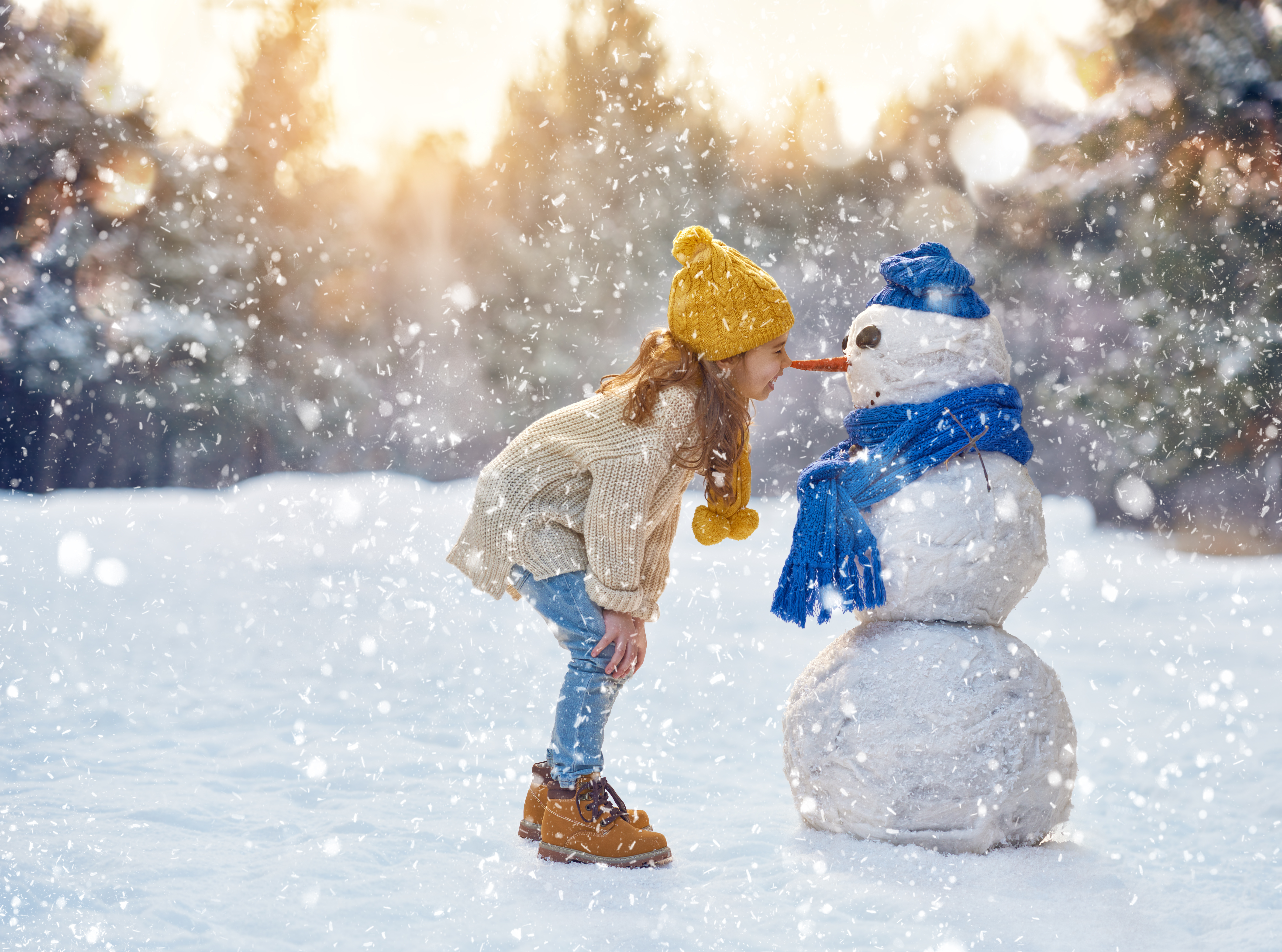 Une fille joue avec un bonhomme de neige sur un chemin enneigé