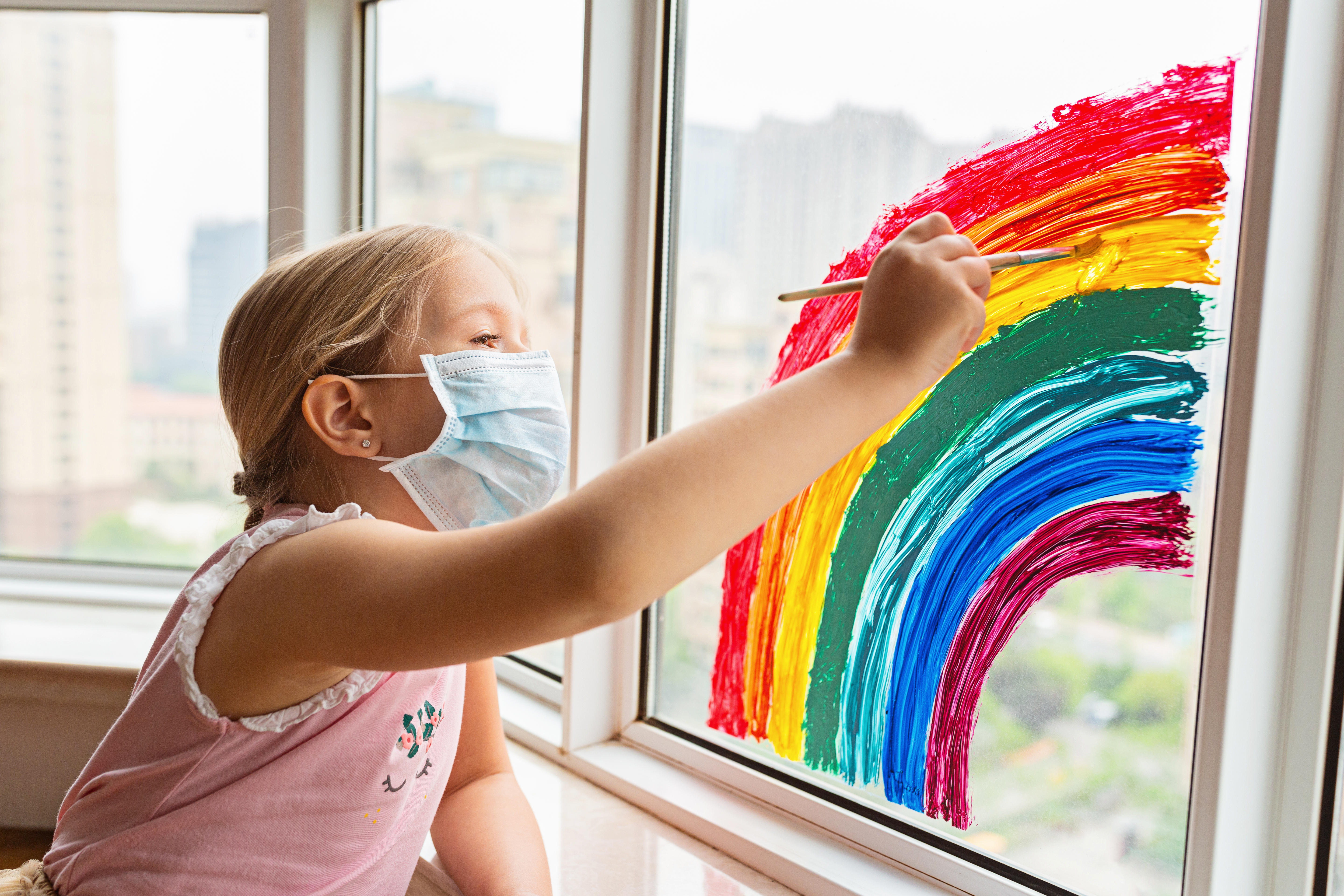 A girl drawing a rainbow on a window.