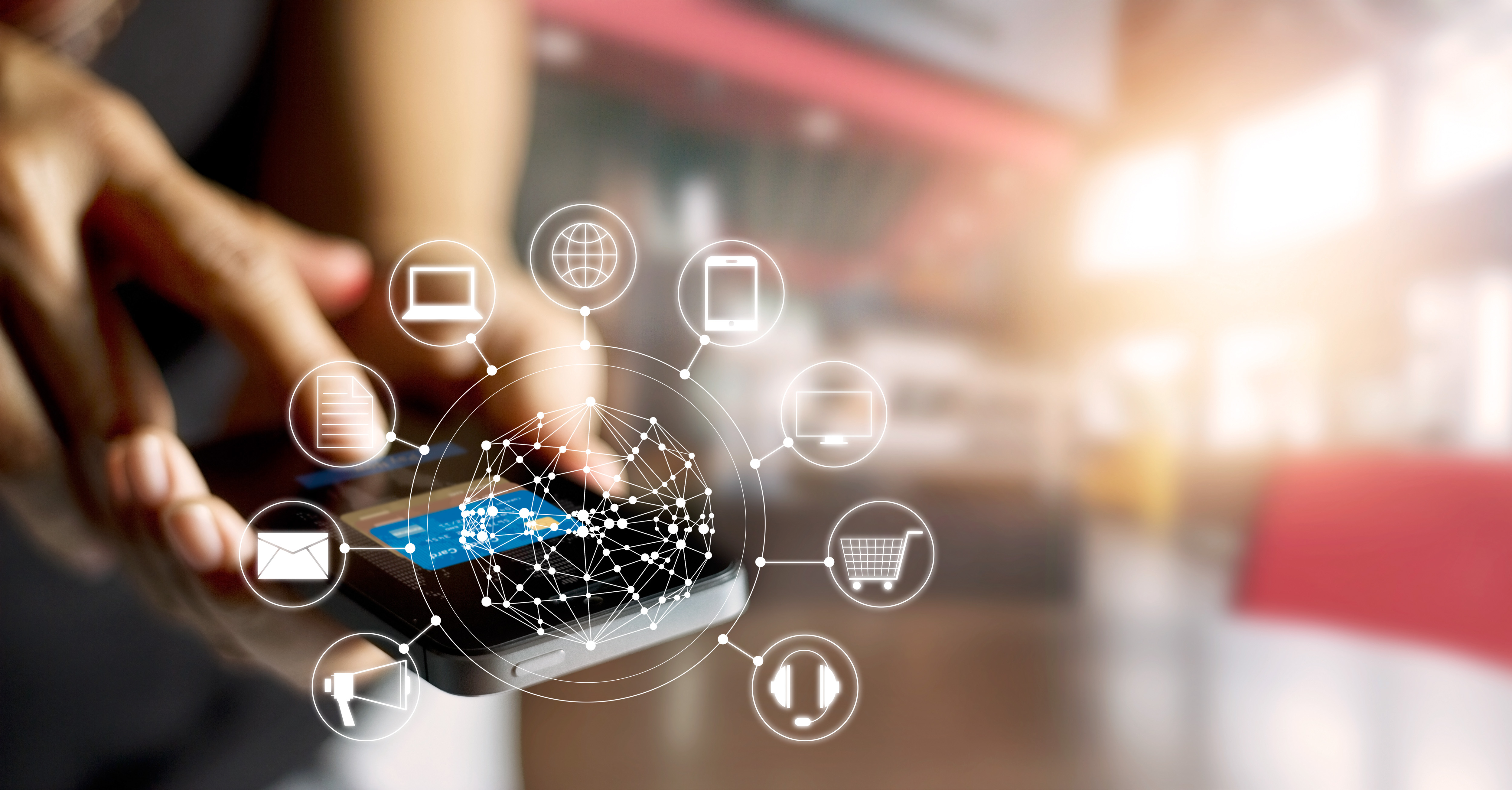 Image d’une main qui tient un téléphone cellulaire à l’arrière-plan d’un graphique qui comprend un diagramme en forme de toile virtuel et des icônes de  mégaphone, enveloppe, bloc-notes, ordinateur portable, globe terrestre, téléphone portable, écran d'ordinateur, panier d'achat, casque d'écoute