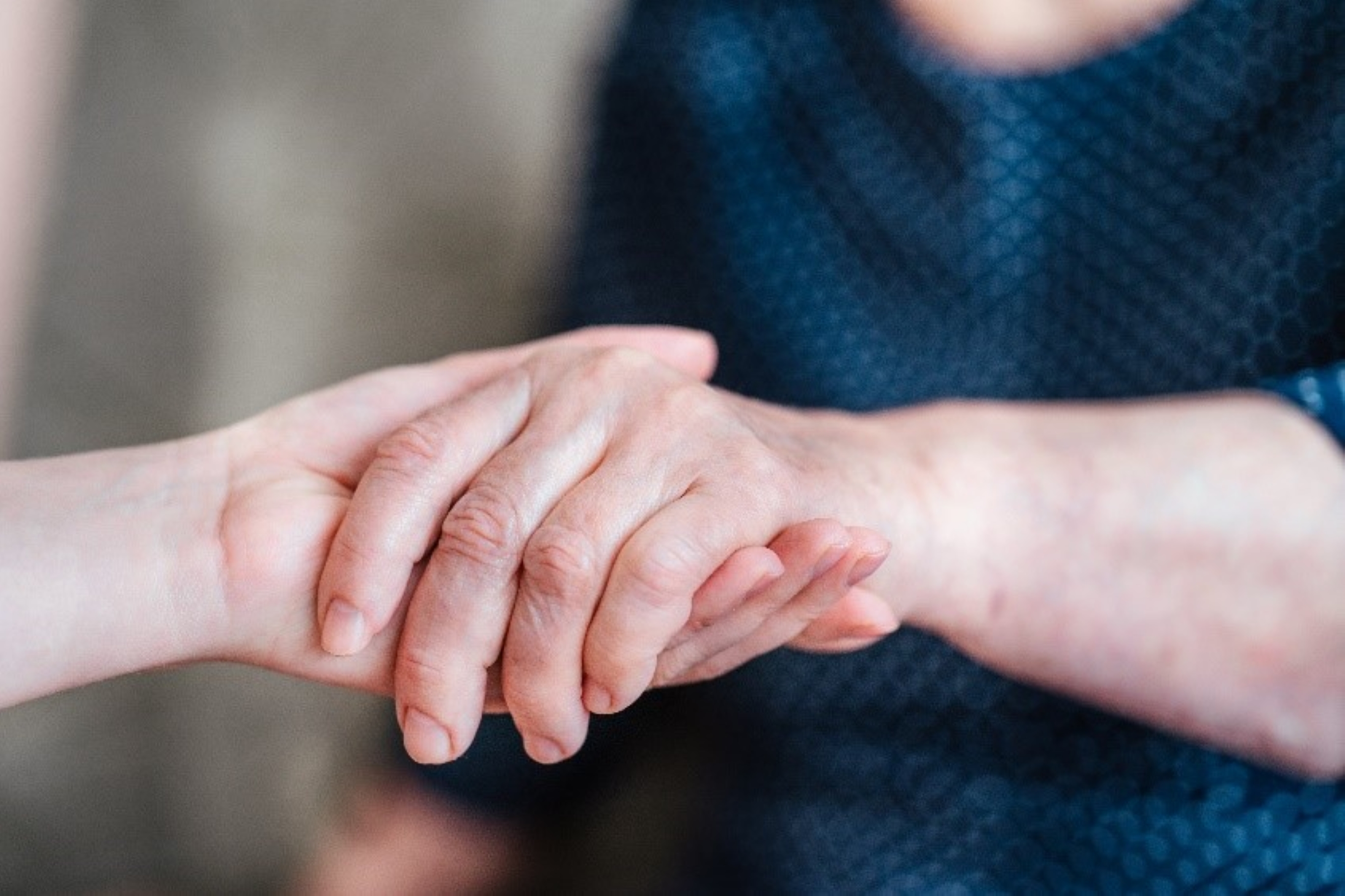 Two hands, belonging to people of different ages, reach out, holding each other.