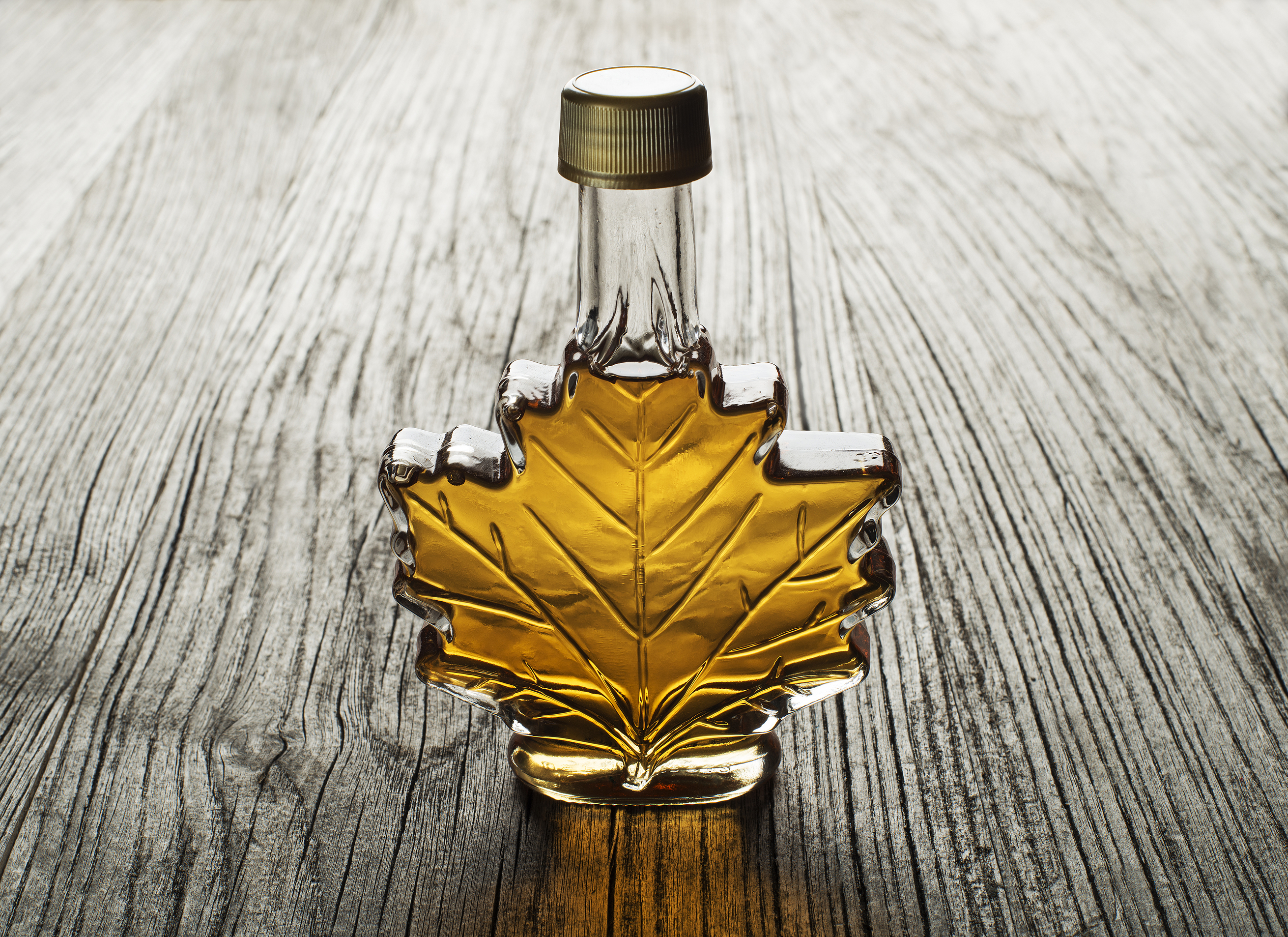 A maple leaf-shaped bottle of maple syrup sitting on a rustic wooden table