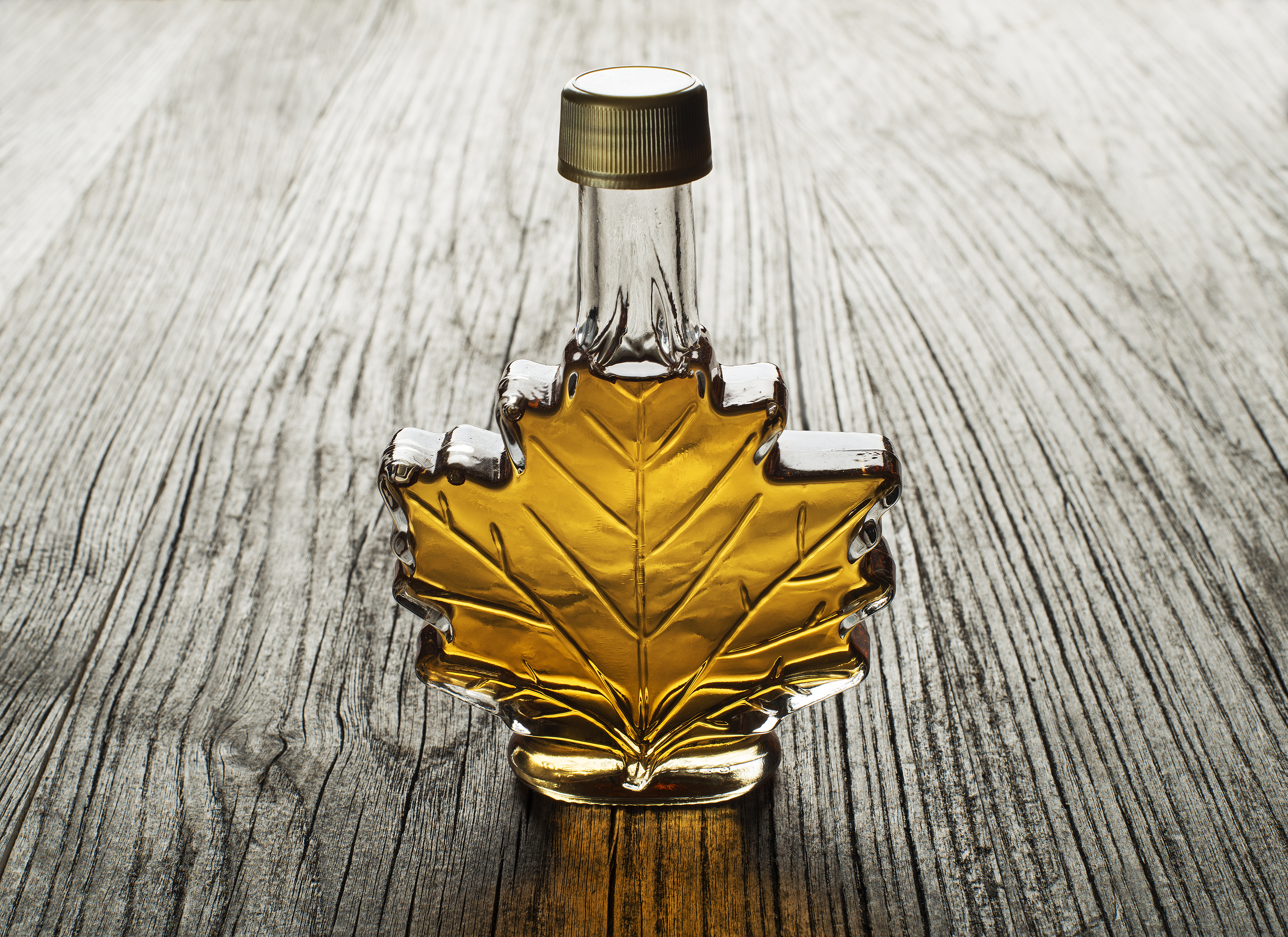 Une bouteille de sirop d’érable en forme de feuille d’érable repose sur une table en bois rustique