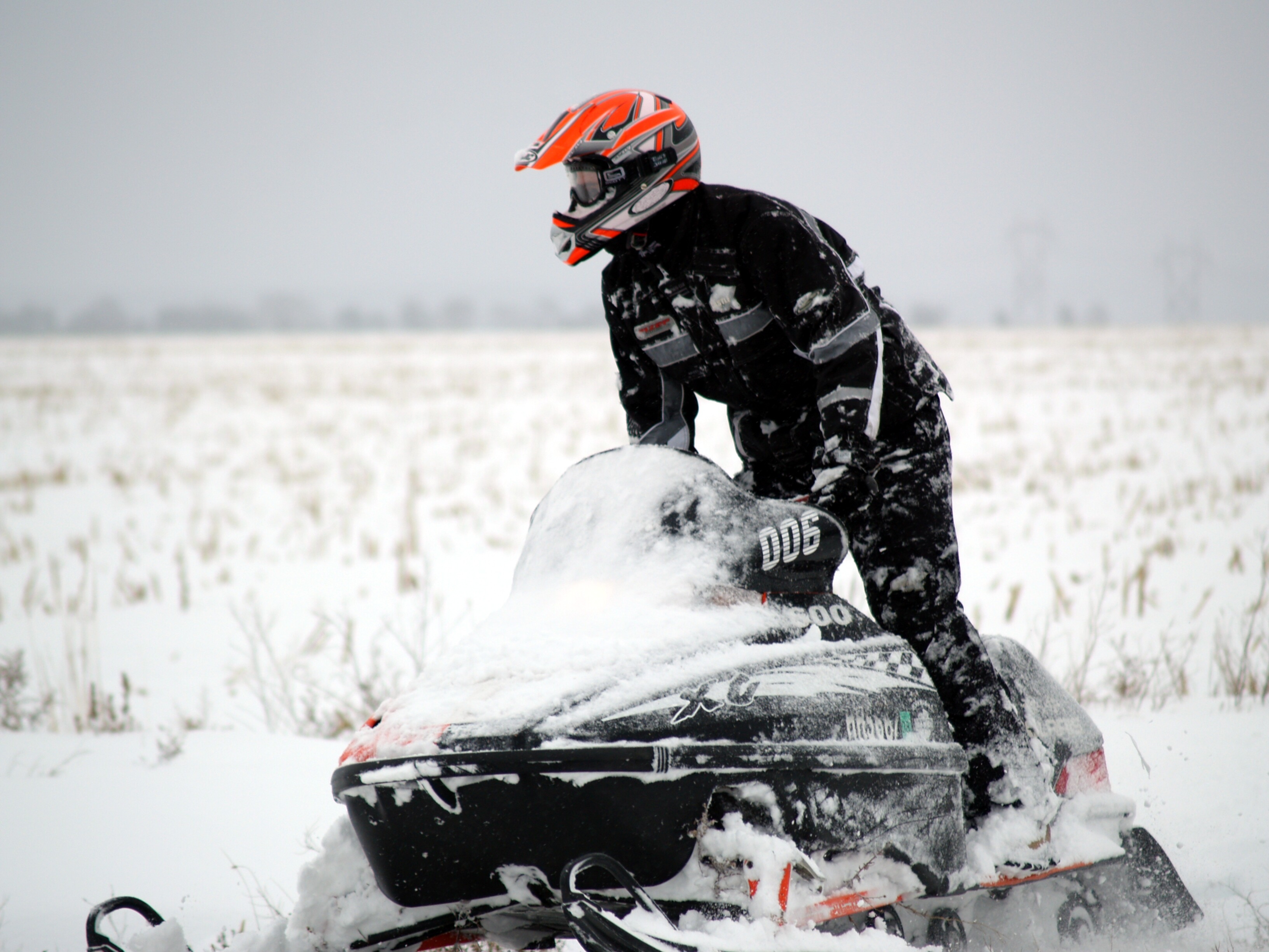 Person driving a snowmobile in a snowy field, while standing.