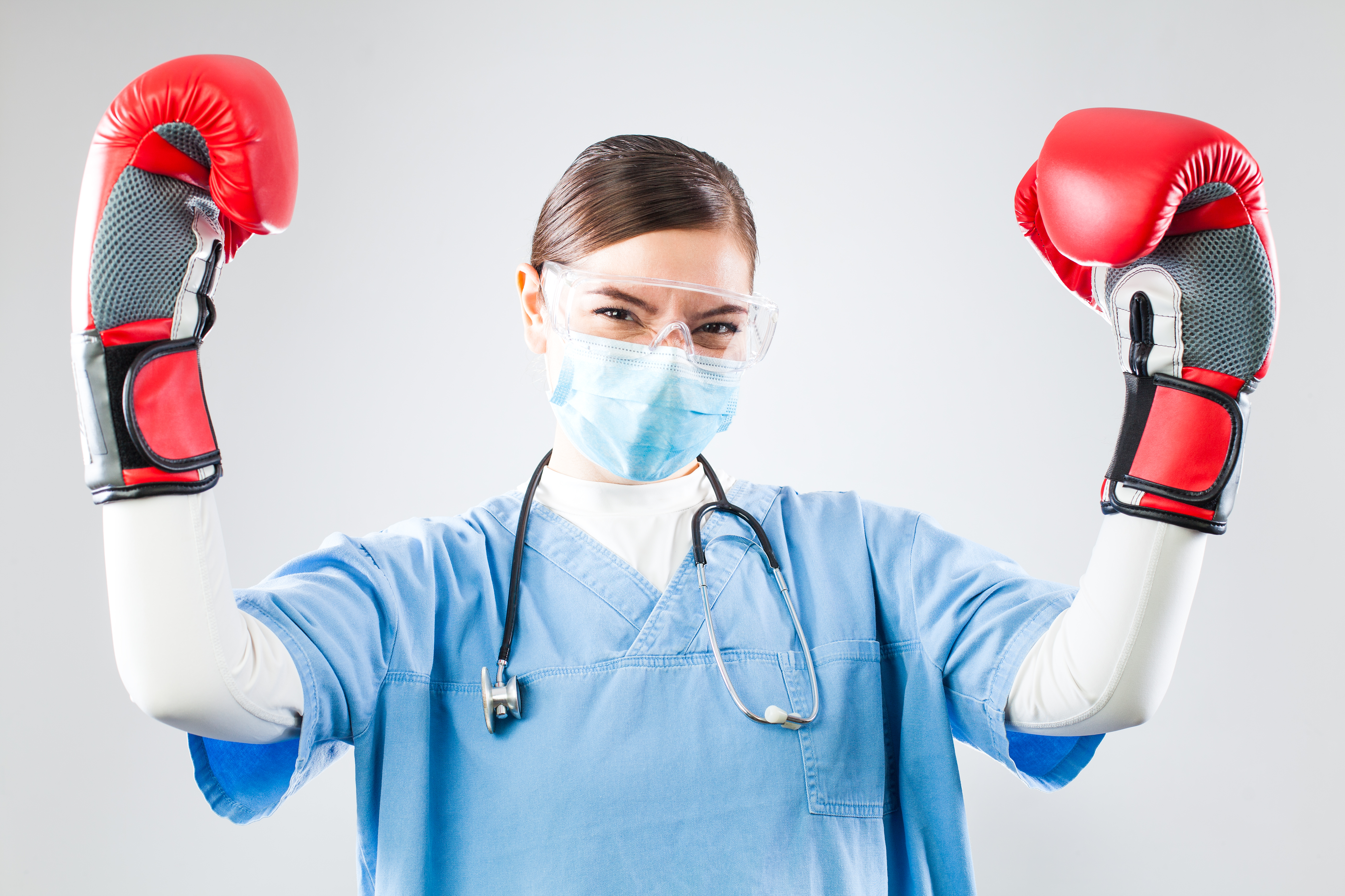 Femme médecin portant des lunettes protectrices, un masque chirurgical et des gants de boxe.