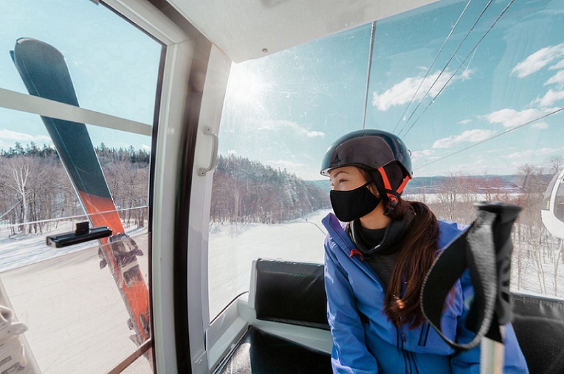 A young woman with ski gear going up a gondola wearing a mask during the pandemic.