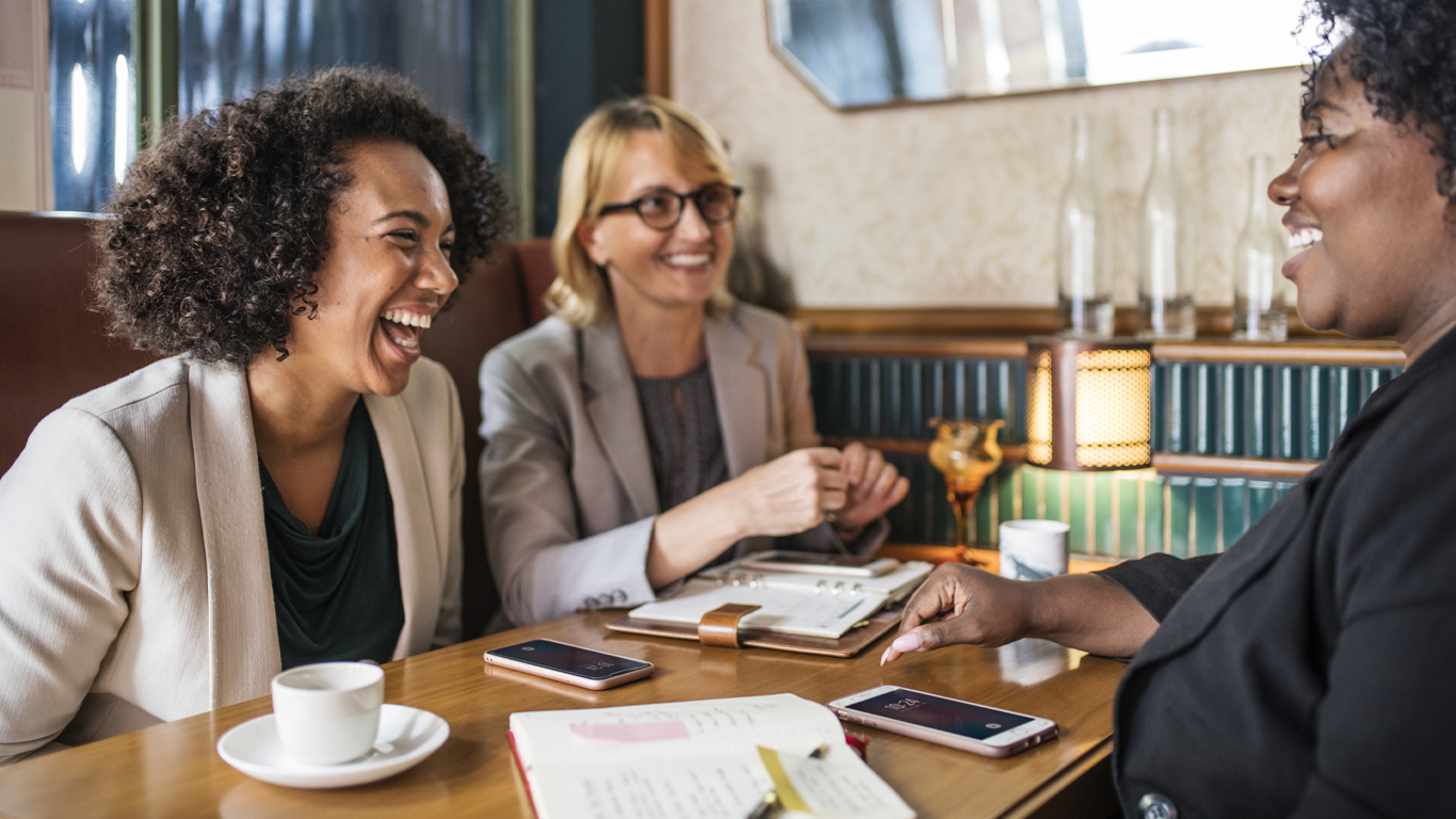 Three women sitting at a table in a café, laughing.