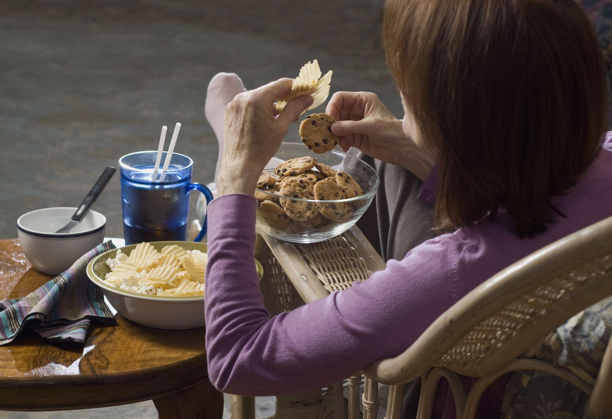 Une femme assise qui mange des croustilles et des biscuits aux brisures de chocolat.