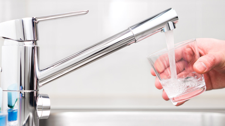 Un homme remplissant un verre d’eau à partir d’un robinet.