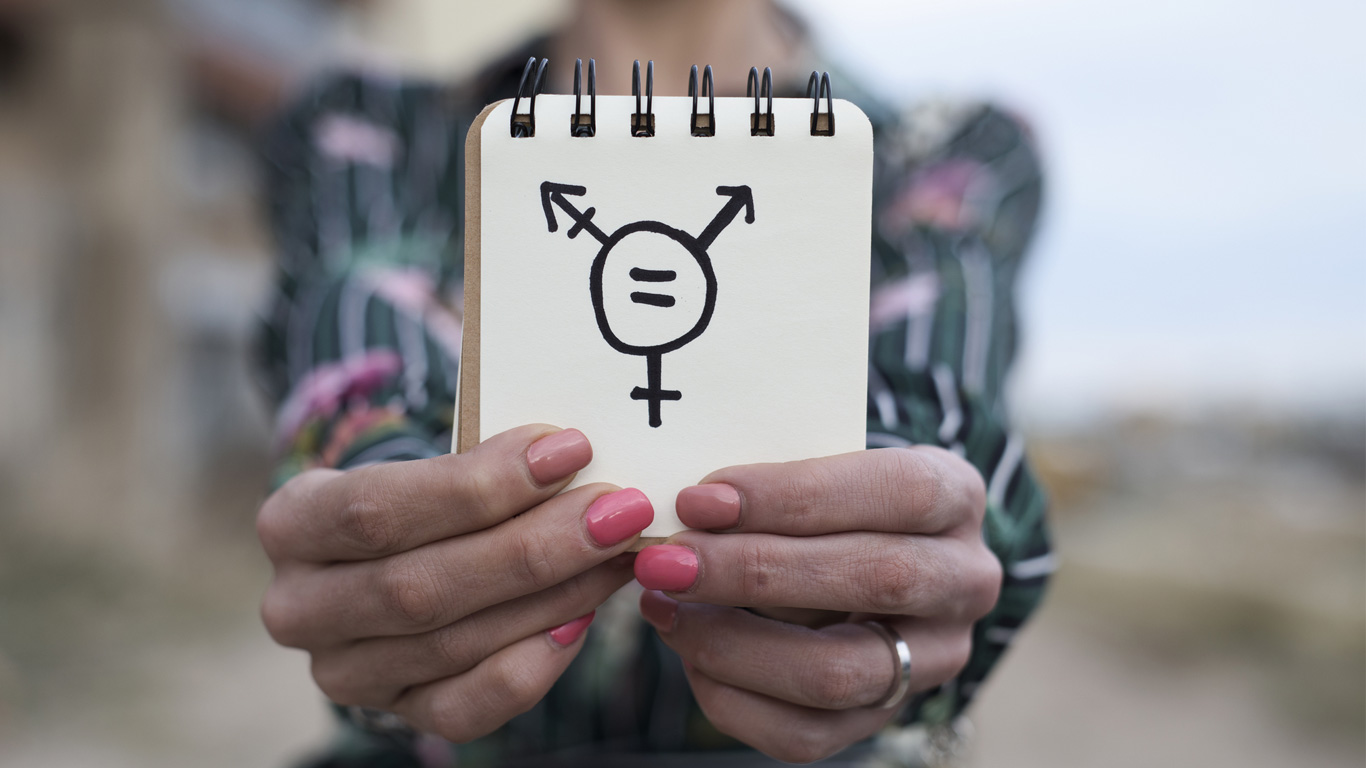 Gros plan d’une personne tenant un bloc-notes sur lequel est dessiné un symbole transgenre.