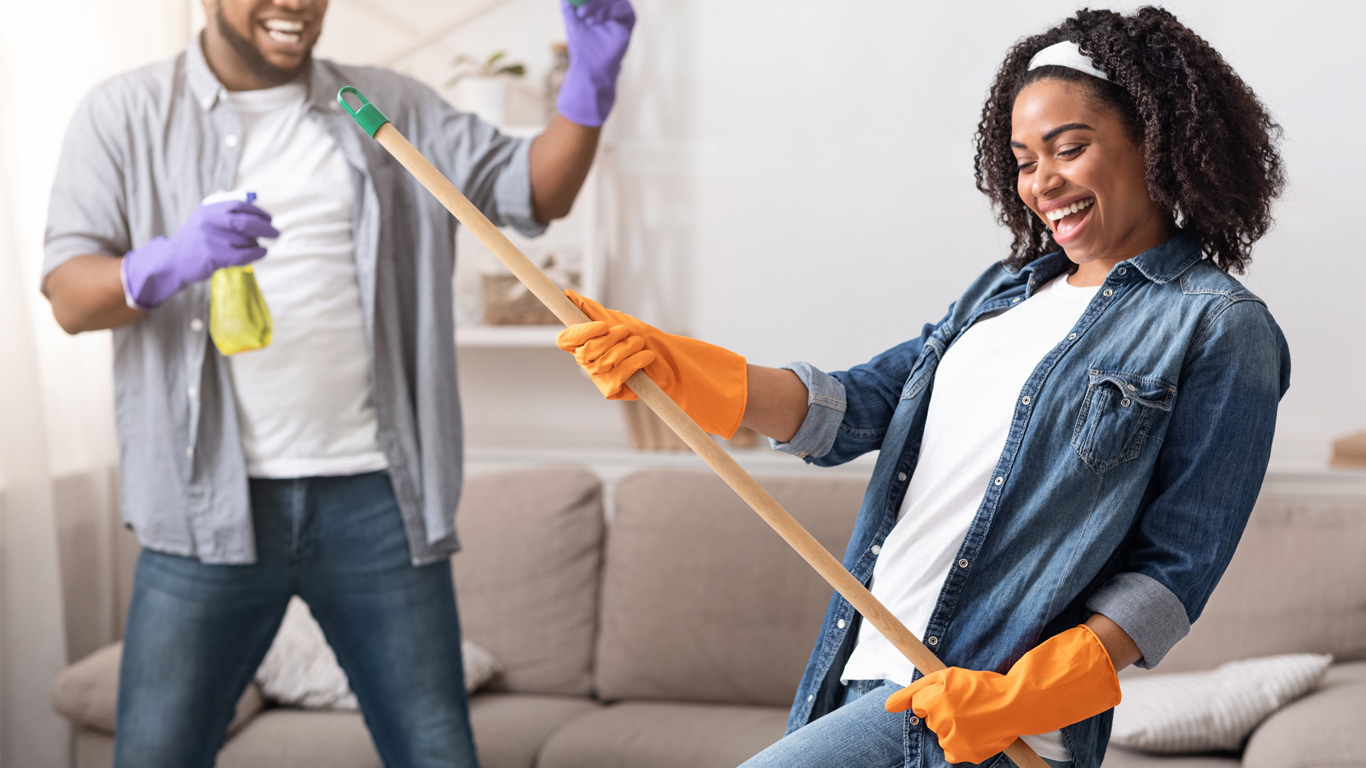 Joyful couple fooling around together while tidying their living room. 