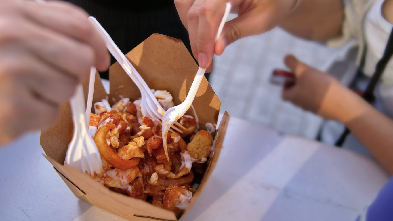 Hands sticking forks into paper box of poutine on table