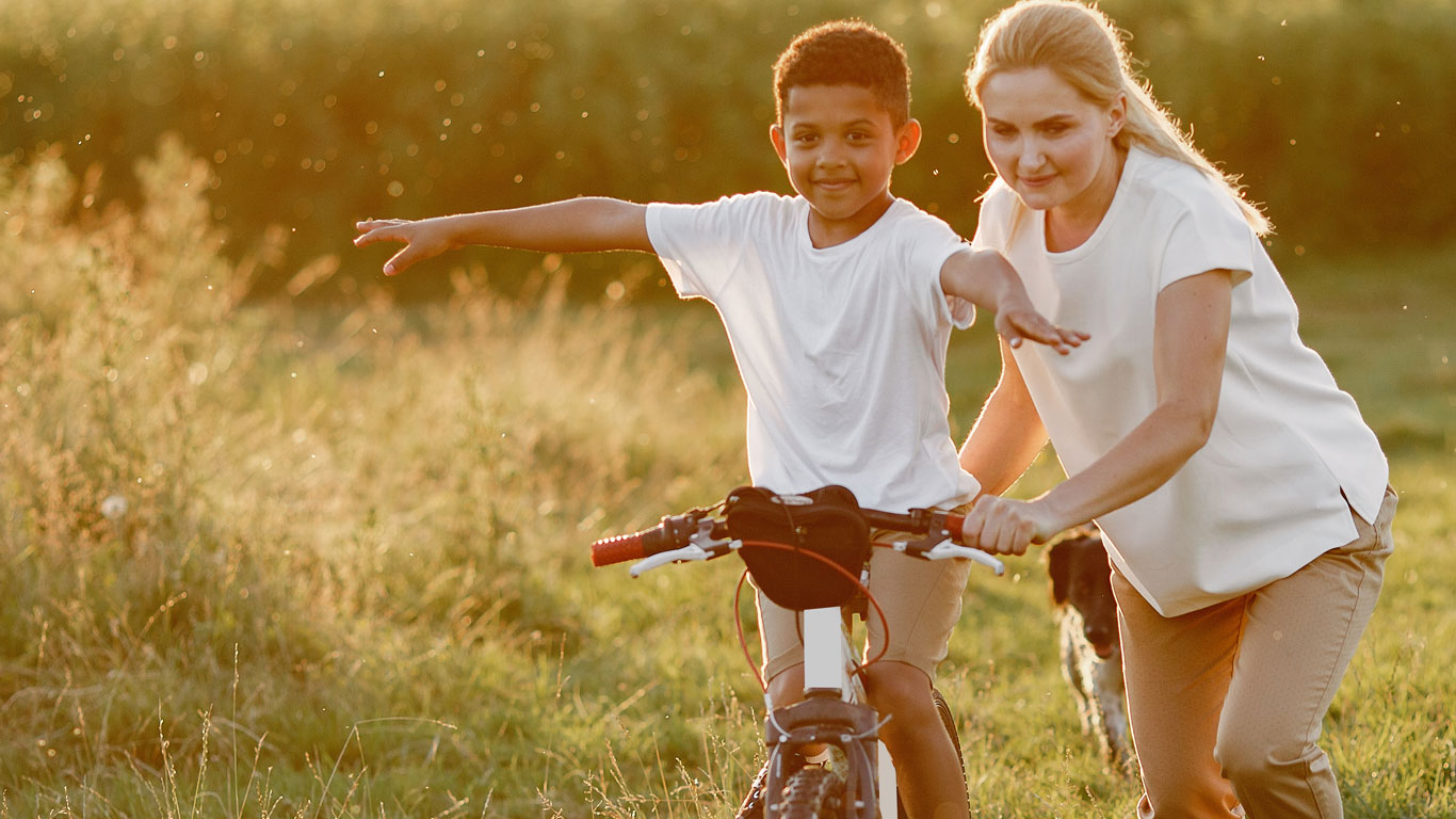 Une femme apprend à un jeune garçon à faire du vélo. 
