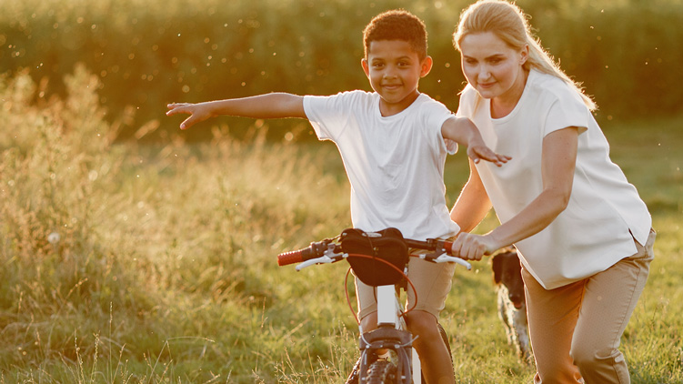 A woman teaching a young boy to ride a bike. 