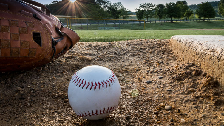 une balle de baseball et un gant sur la terre à côté du monticule du lanceur dans un parc communautaire.