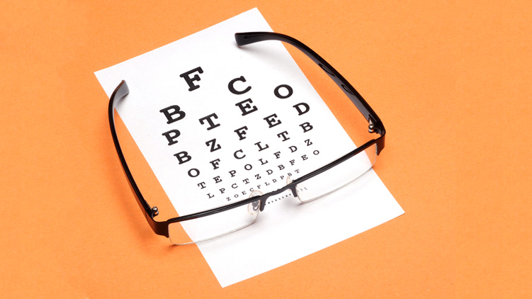 Eye glass with eye exam chart on orange background.