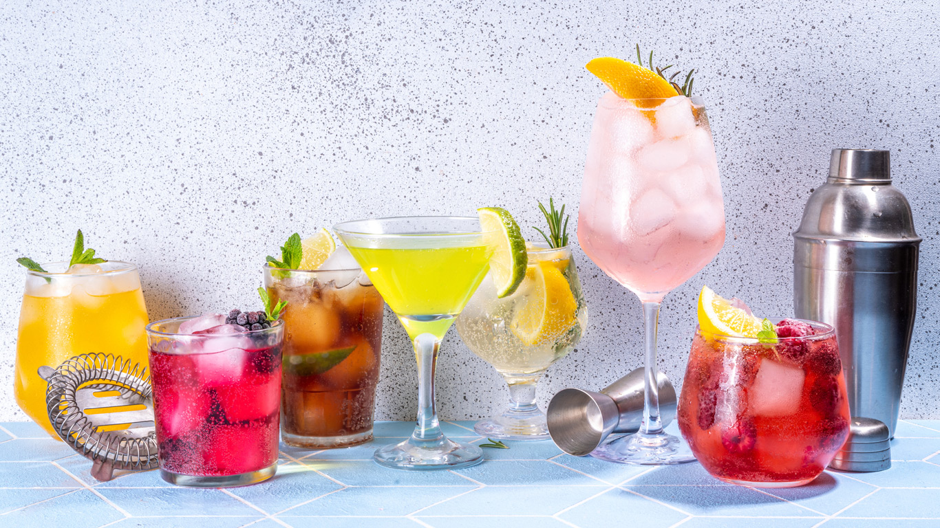 A variety of cocktails are arranged on a table with a cocktail shaker.