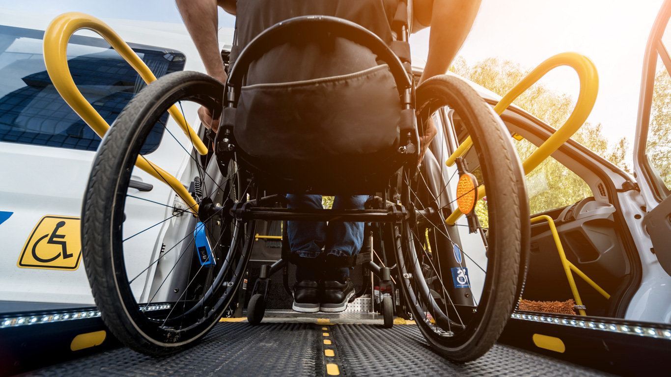 Une personne en fauteuil roulant qui monte dans un véhicule de transport à l’aide d’une rampe d’accès pour fauteuil roulant.