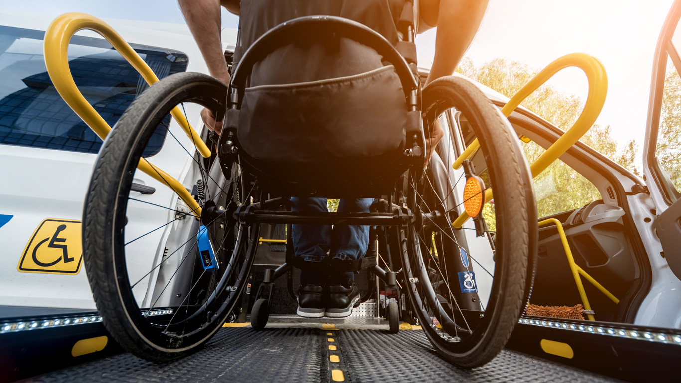 A person in a wheelchair getting into a transport vehicle using a wheelchair access ramp.