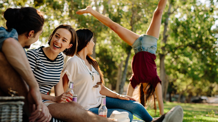 people sitting and talking in a park, person doing a cartwheel in the background.