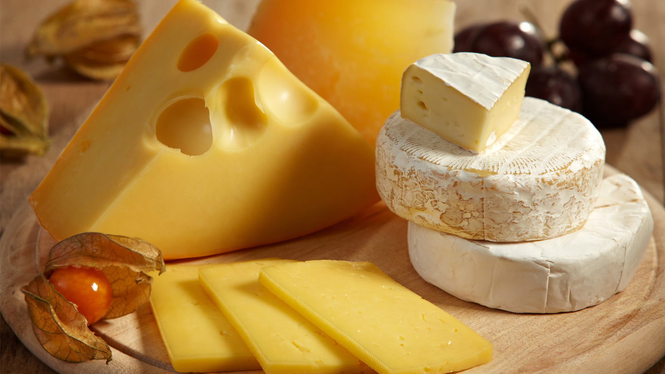 cheese and fruits on wooden cutting board.