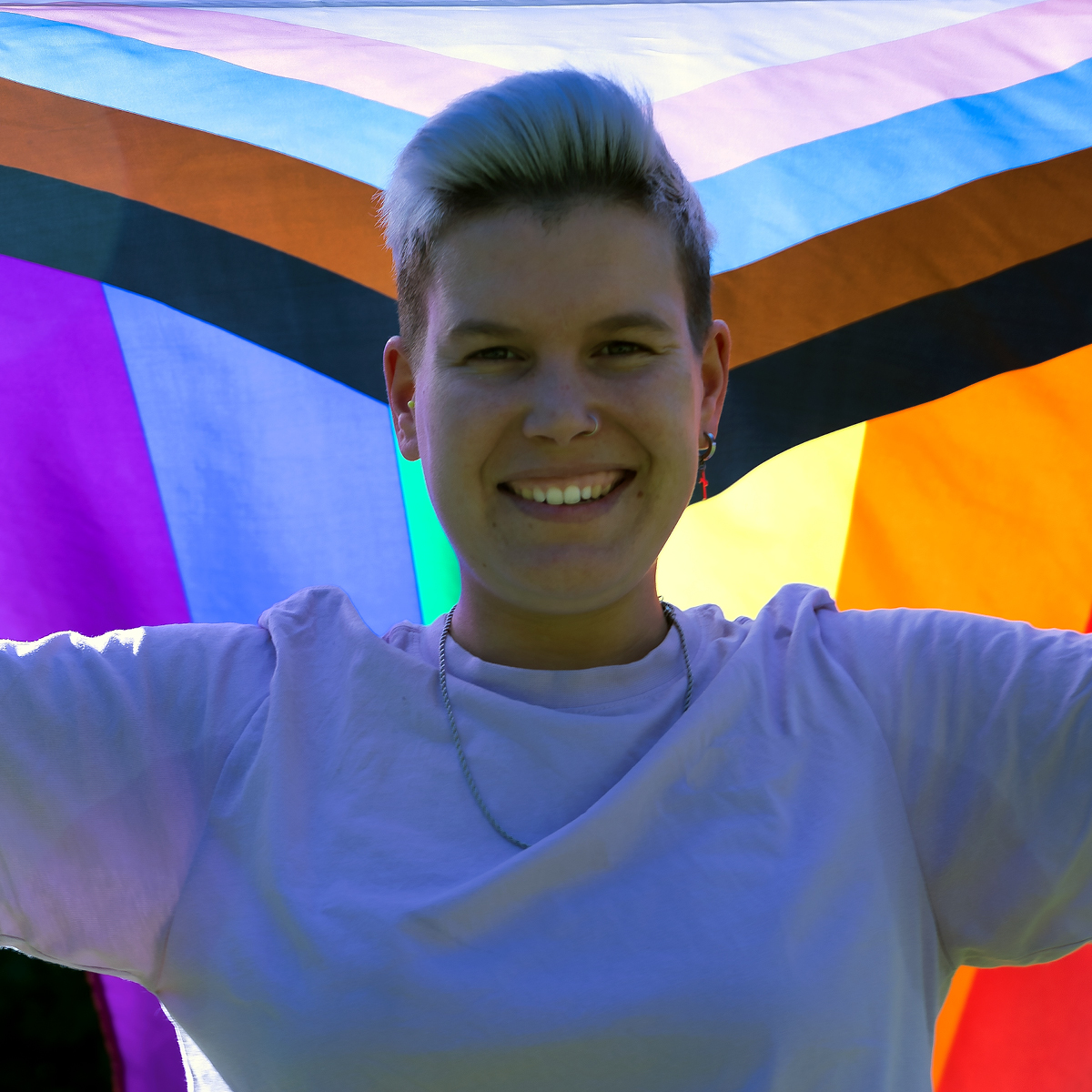 Portrait of a non-binary person raising an LGBTQ2+ community flag.