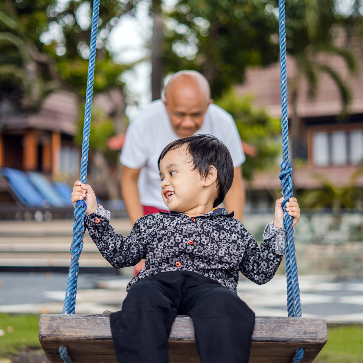 Grandfather pushing their grandchild on a park swing.