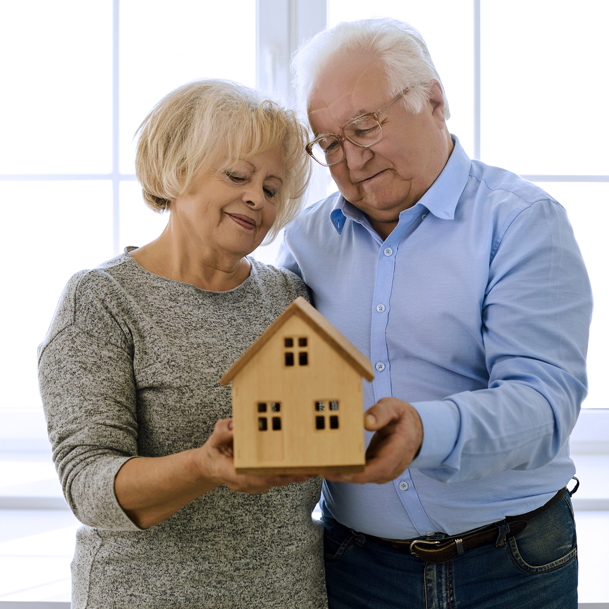 Smiling senior couple looking at a wooden model of a house being held in their hands