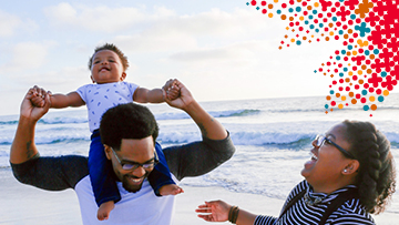 Man and woman on the beach. The man has a smiling baby on his shoulders